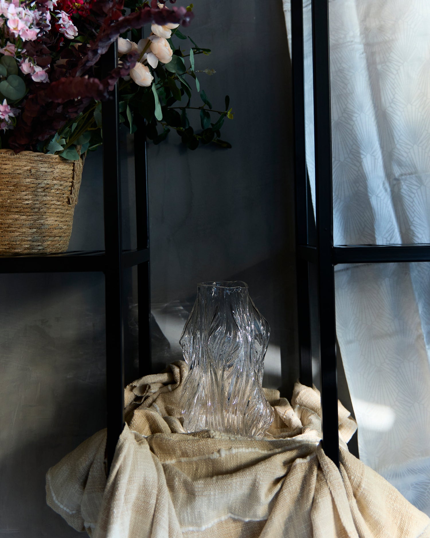 Clear glass vase on a draped surface with a dark background and floral arrangement.